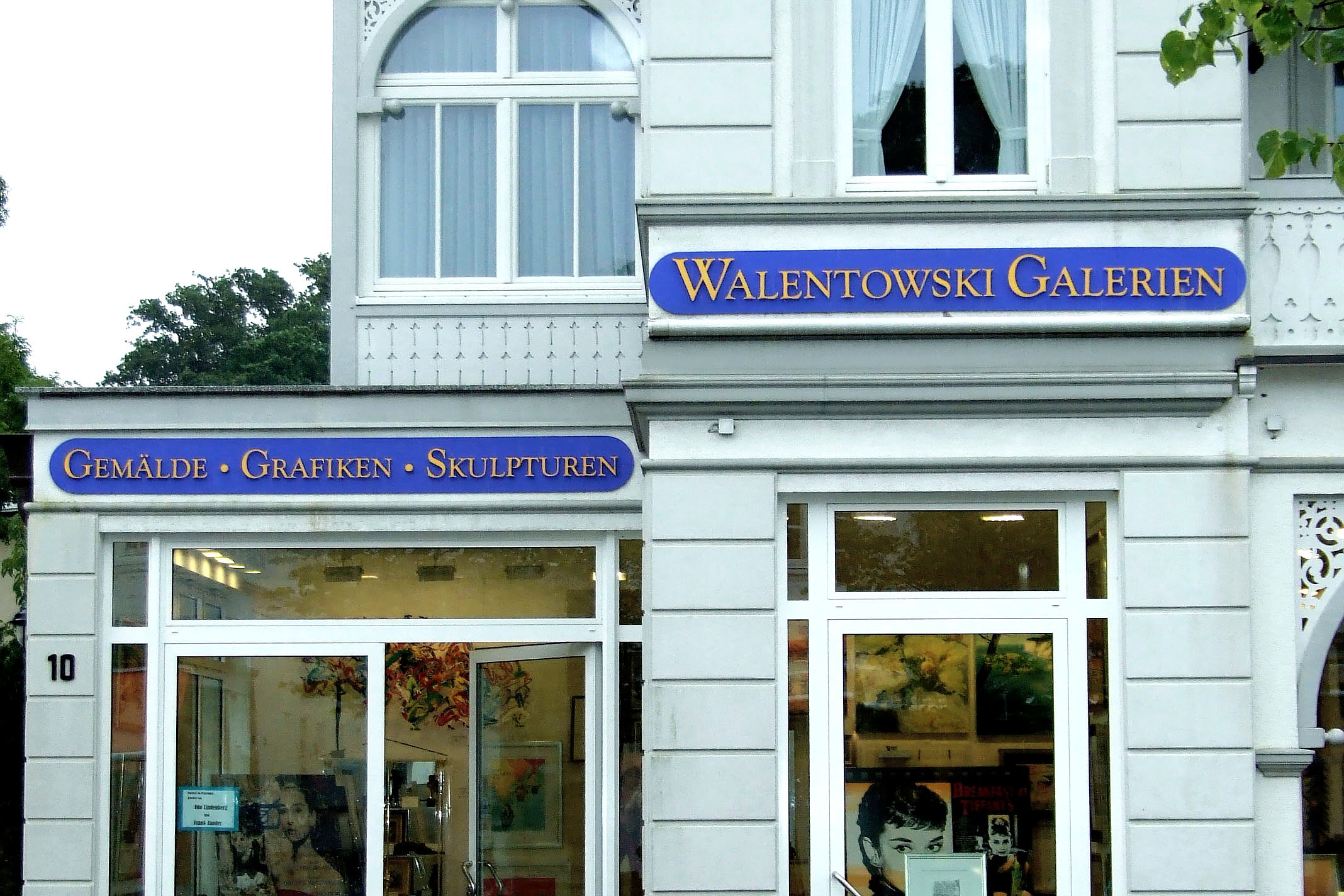 Zwei gewoelbte blaue Fassadenschilder der Walentowski Galerien mit goldener Schrift an weisser Bäderarchitektur